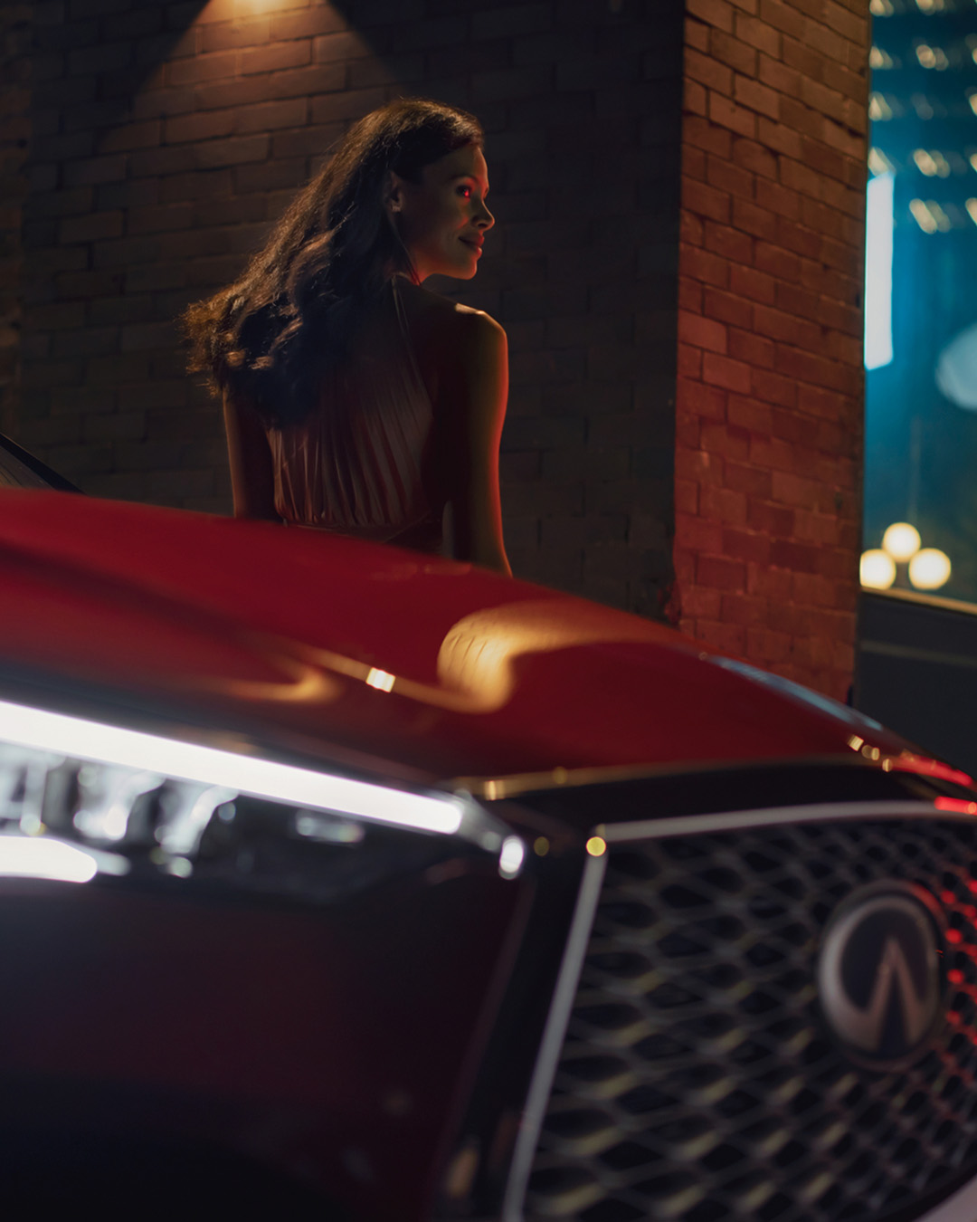 INFINITI vehicle at night with illuminated headlight and woman exiting in upscale city setting