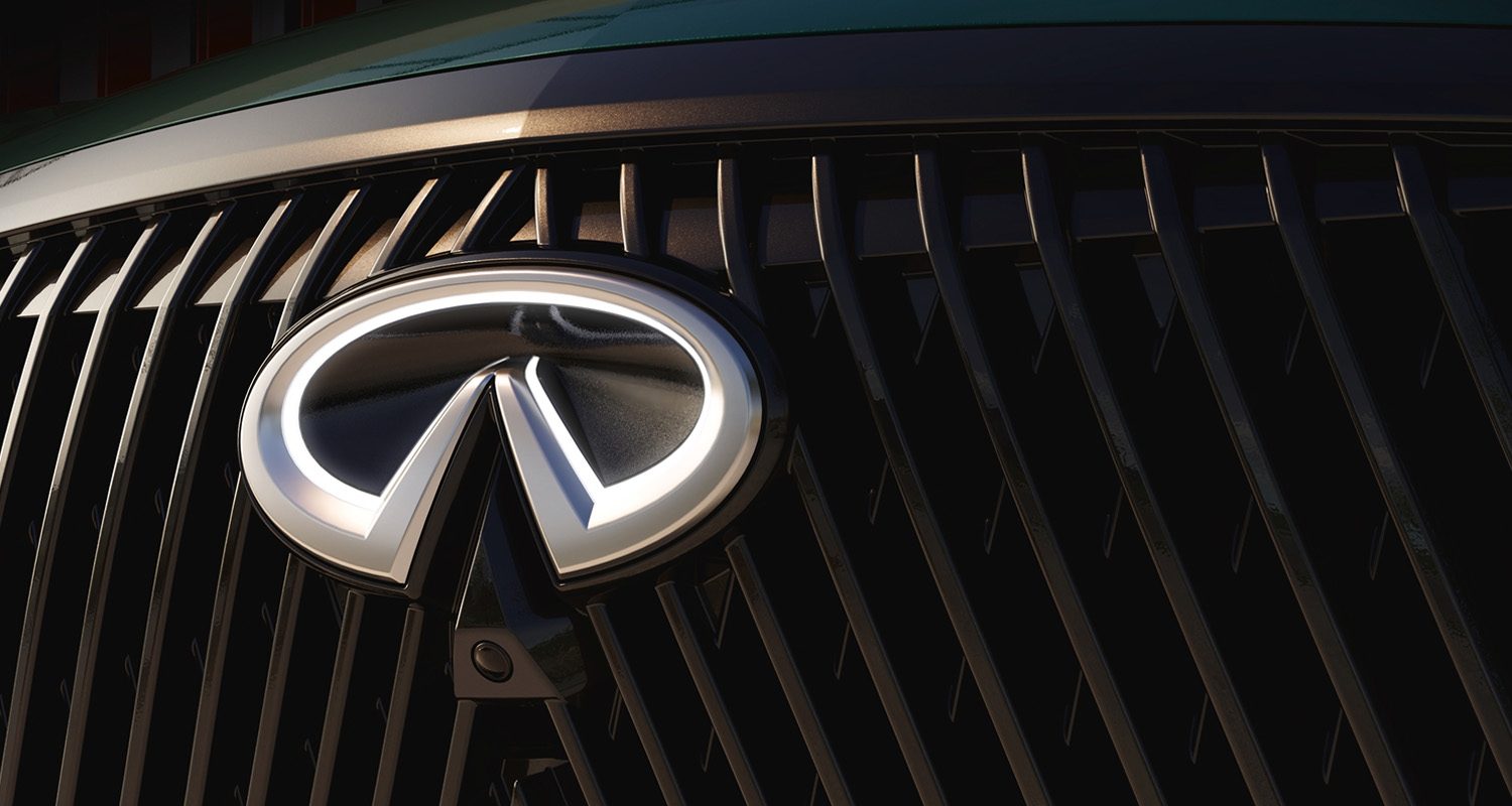 Detailed close-up of illuminated INFINITI emblem and black vertical grille of new QX60 in natural light
