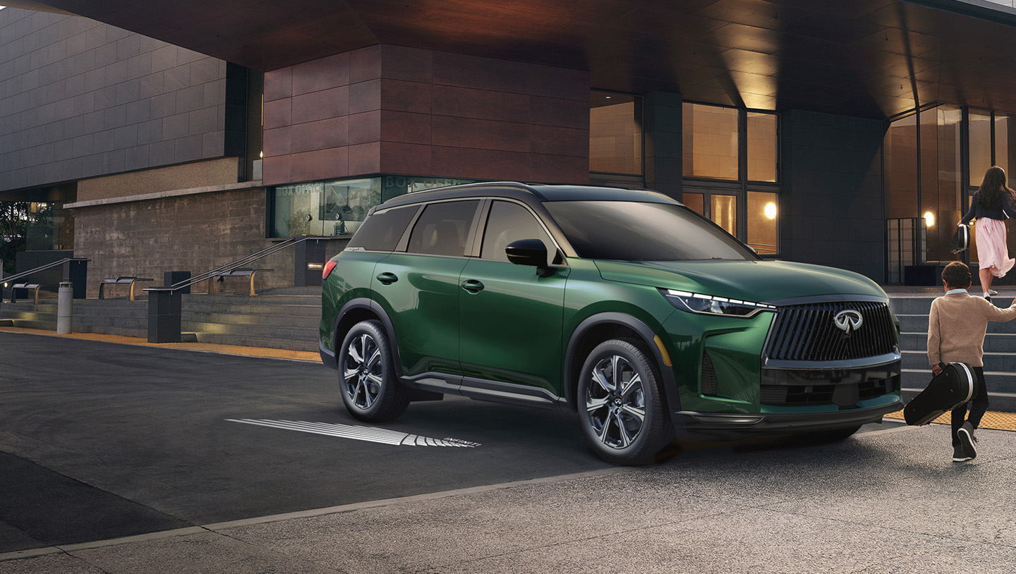 New INFINITI QX60 in Deep Emerald Green parked in front of a theater entrance at dusk with family approaching