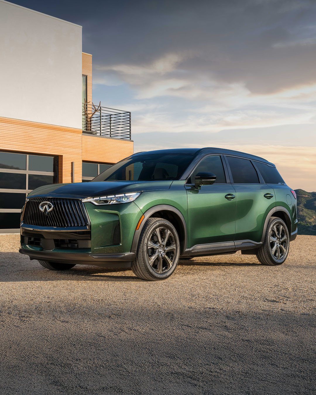 Front side profile of INFINITI QX60 in green parked in front of house at dusk 