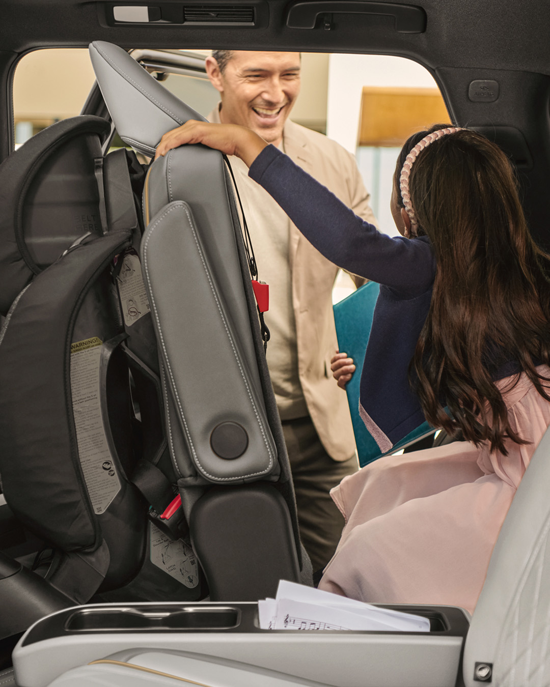Girl activating third-row access with one-touch seat release while adult smiles in background