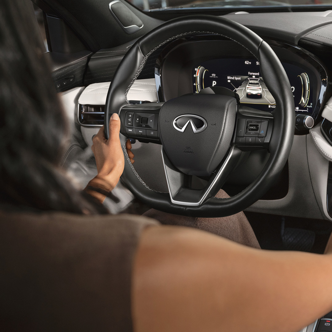 Driver behind wheel of 2026 INFINITI QX60 viewing instrument cluster with active driver assist features