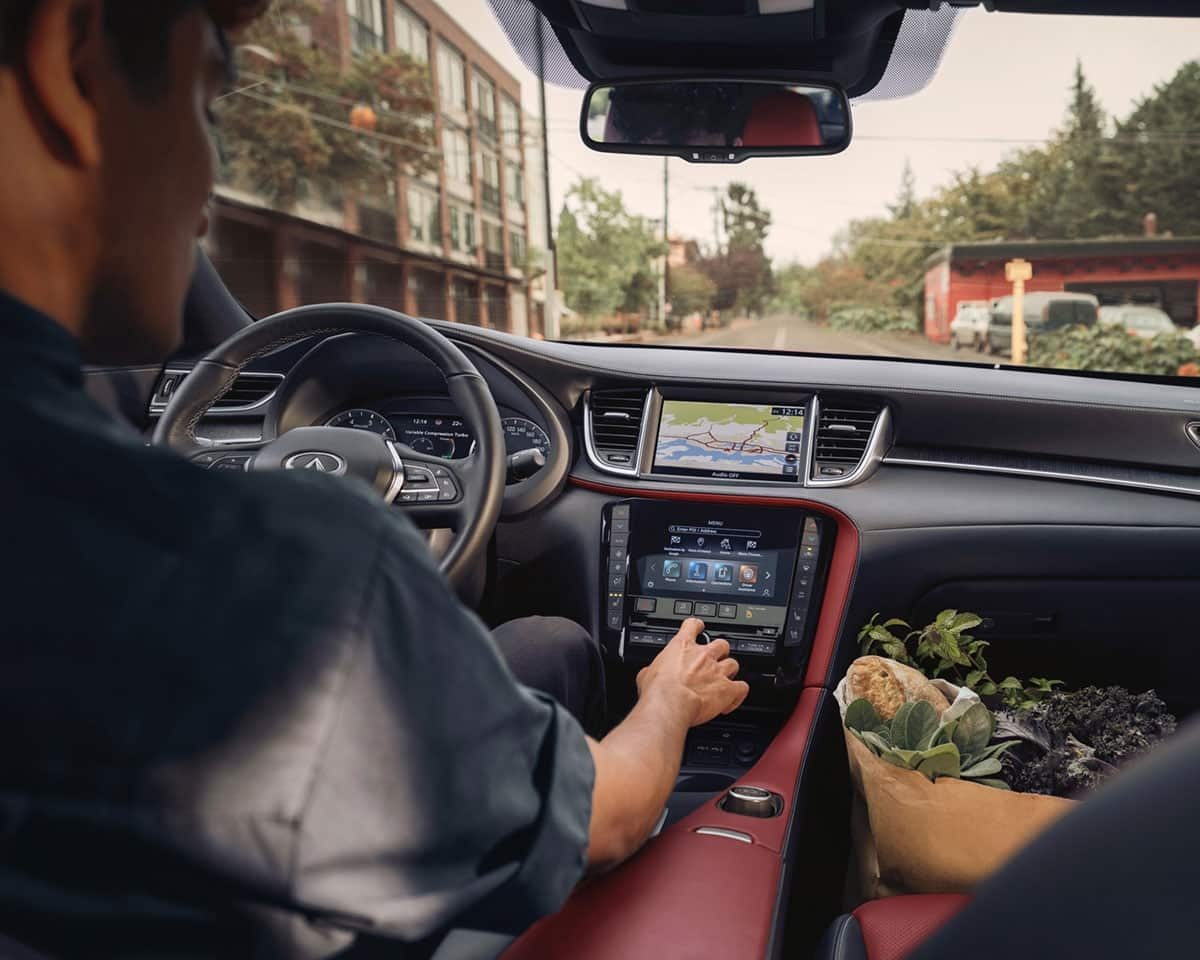 גבר נוהג באינפיניטי QX55 ומשתמש בצמד מסכי מגע של מערכת מולטימדיה