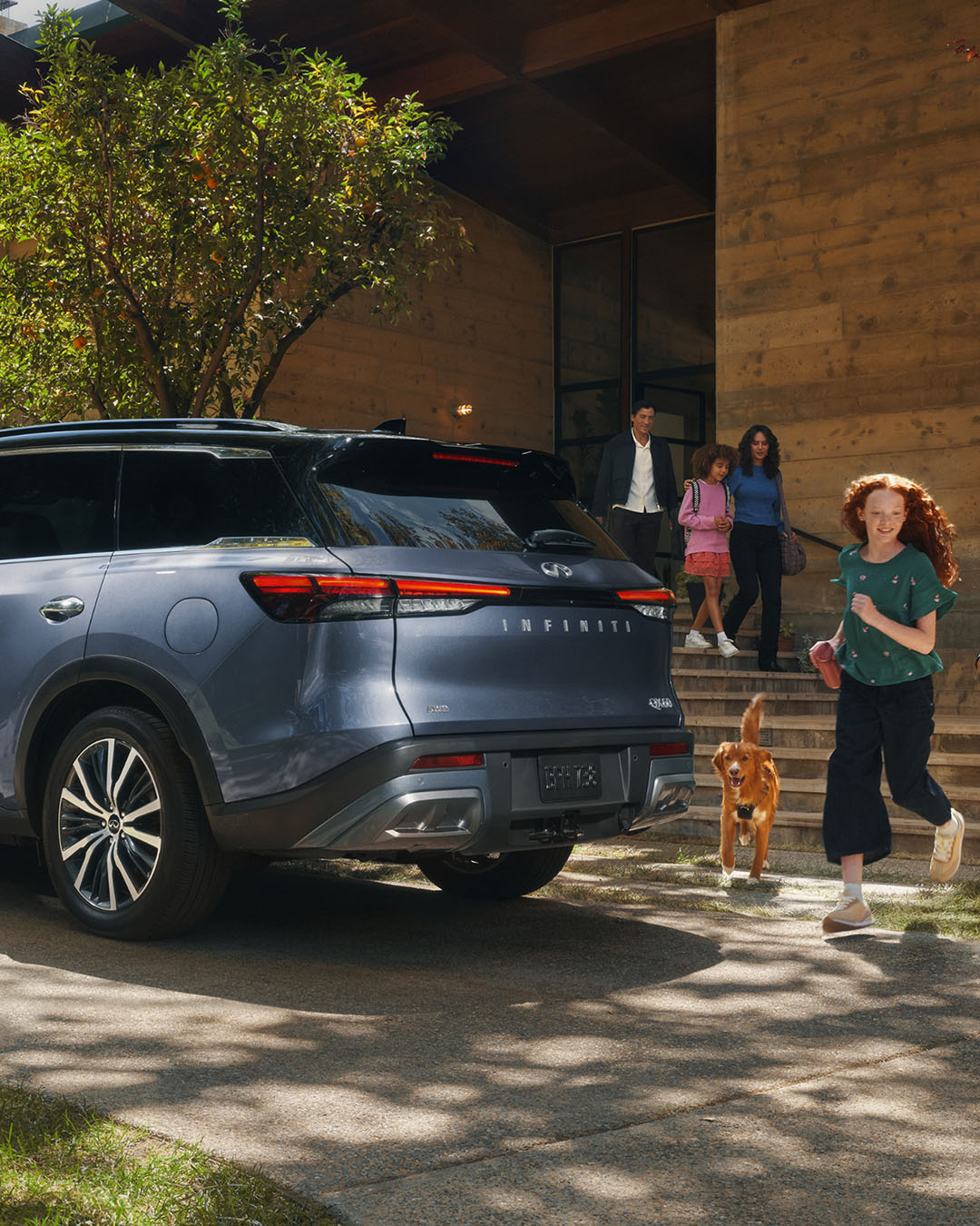 INFINITI SUV parked outside a home with a family and their dog nearby, showcasing the vehicle's versatility