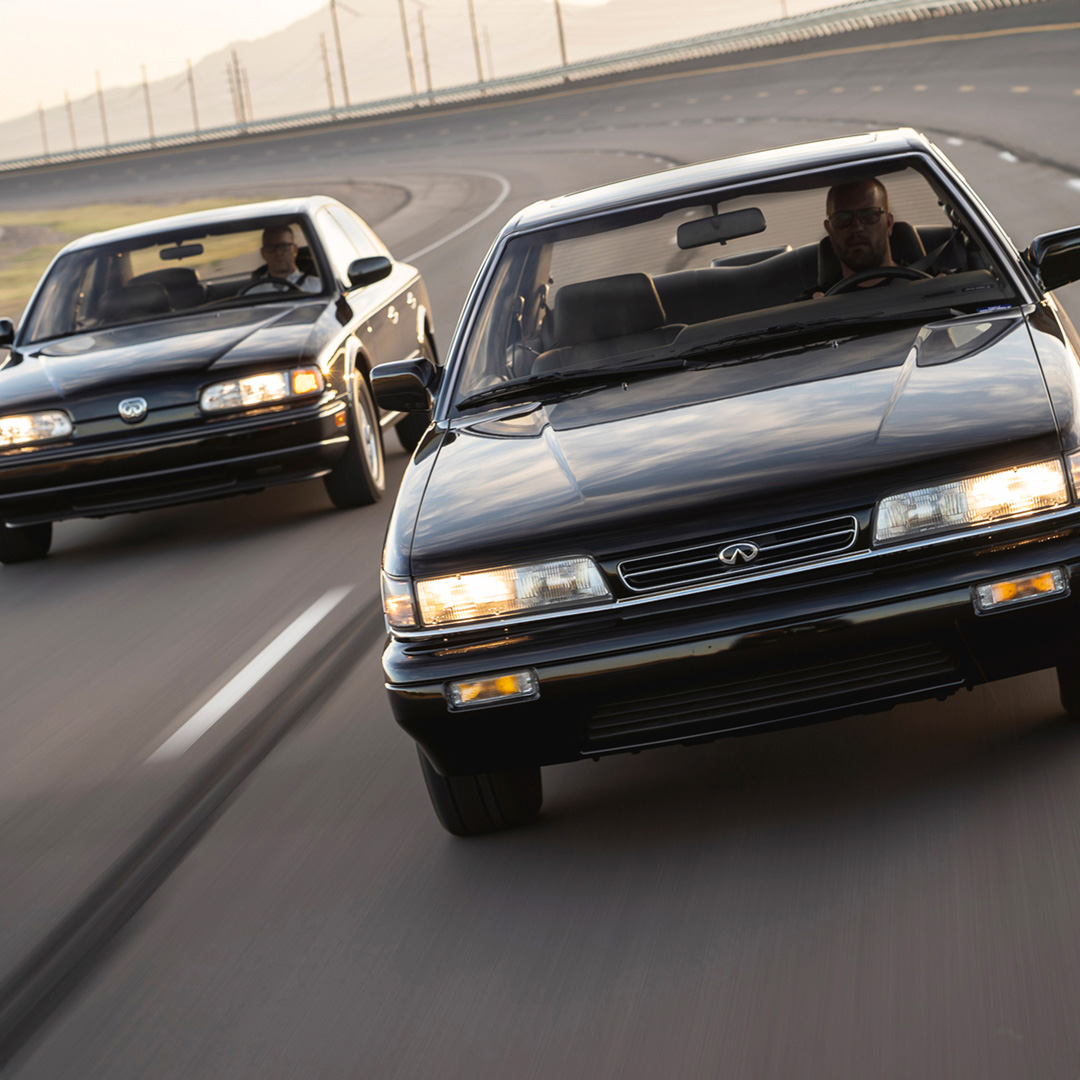 Two INFINITI legacy vehicles driving side by side on race track 