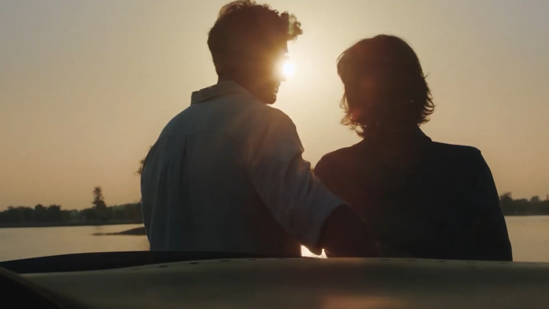 Man and woman watching sunset while leaning on INFINITI vehicle