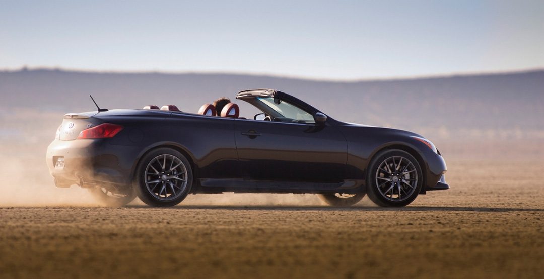 Side view of INFINITI G37 luxury convertible driving across dirt terrain