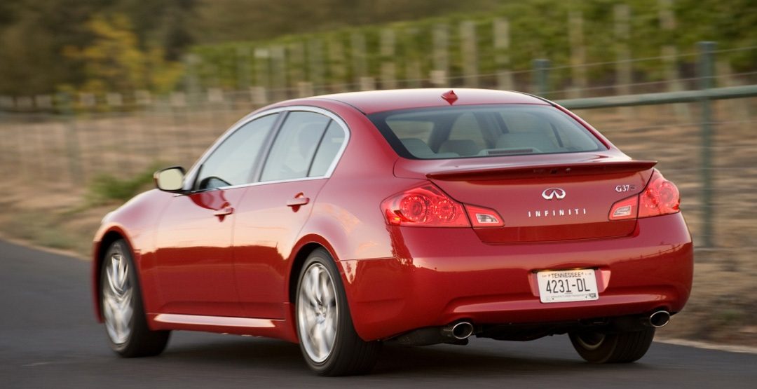Rear view of INFINITI G37 luxury sport sedan in red driving past fence