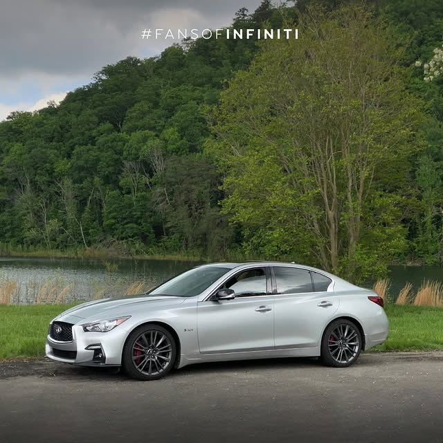 Gray INFINITI Q50 on a lakeside road with greenery