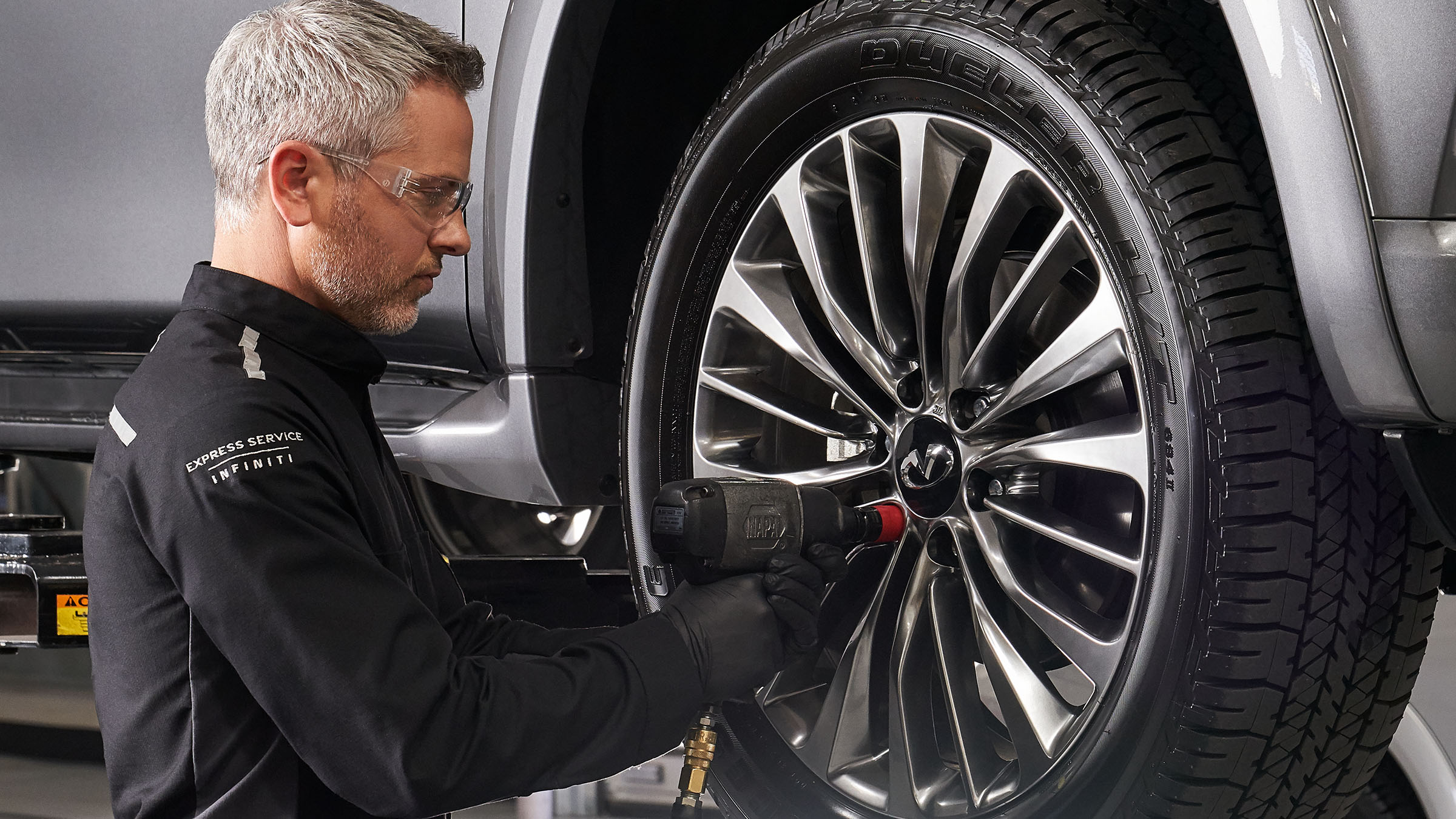 An auto repair mechanic checking the wheel of a 2022 INFINITI vehicle.