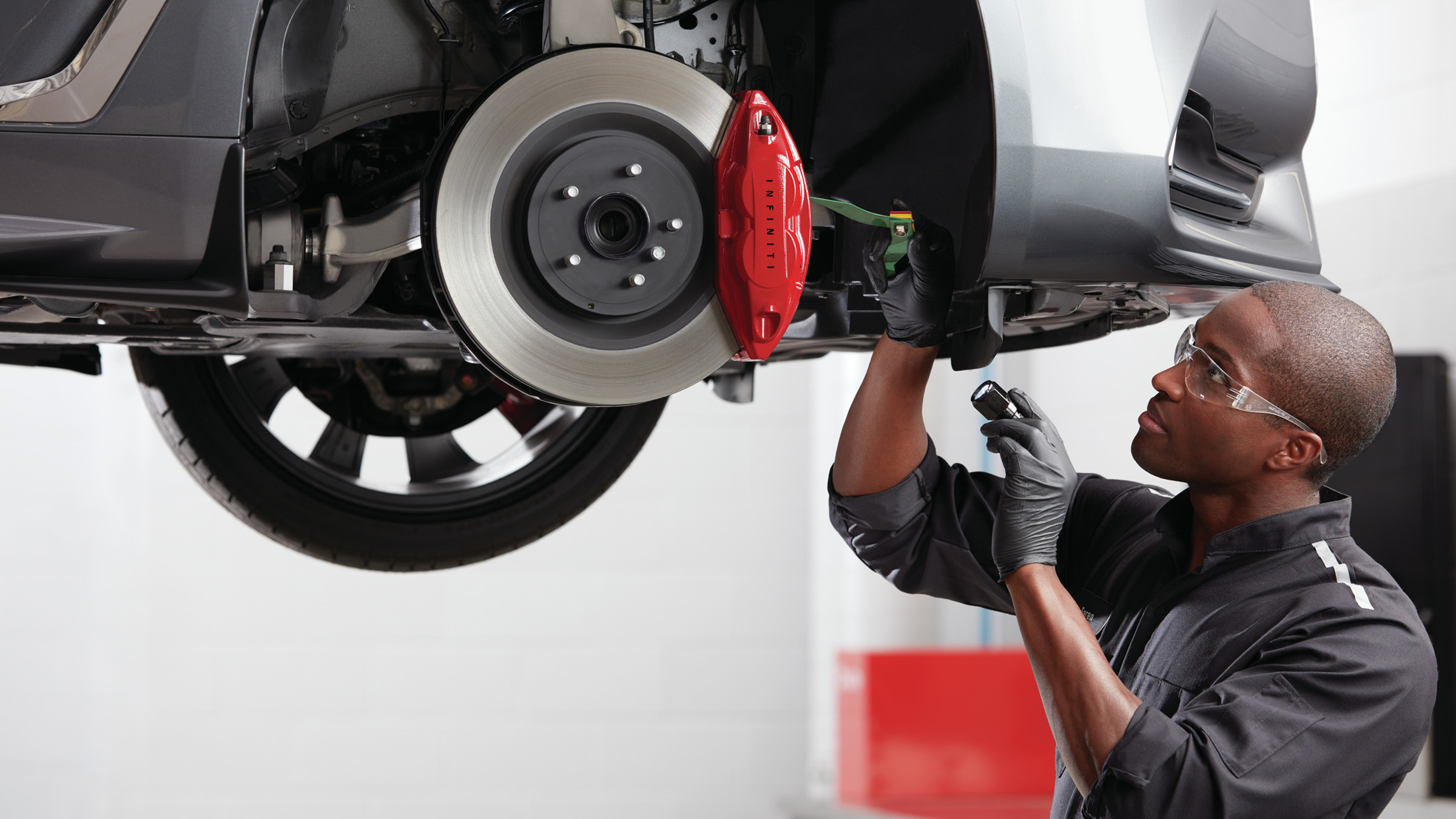 An auto repair mechanic checking under a 2022 INFINITI vehicle.