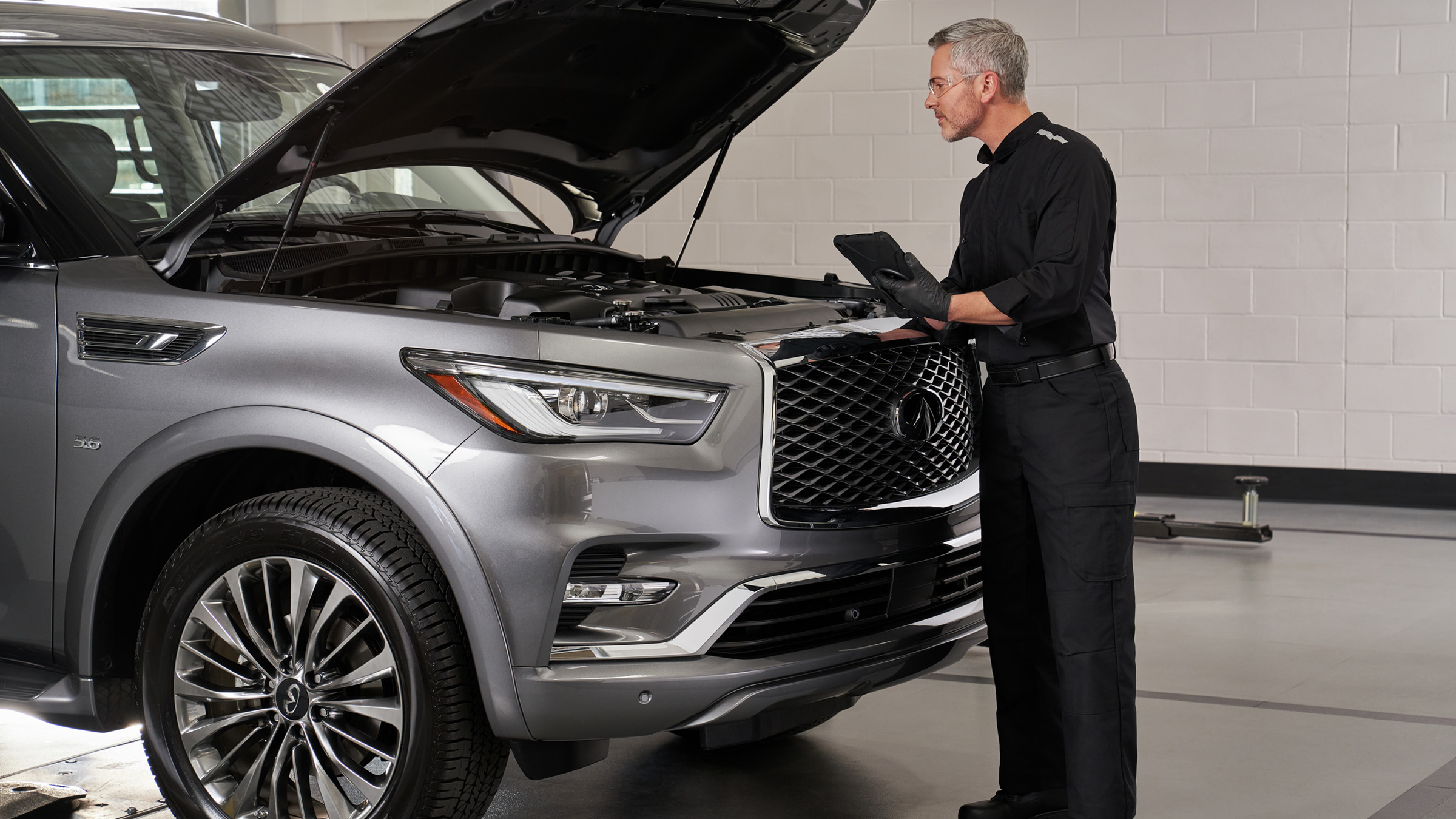 An auto repair mechanic checking under the hood of the 2022 INFINITI QX80.